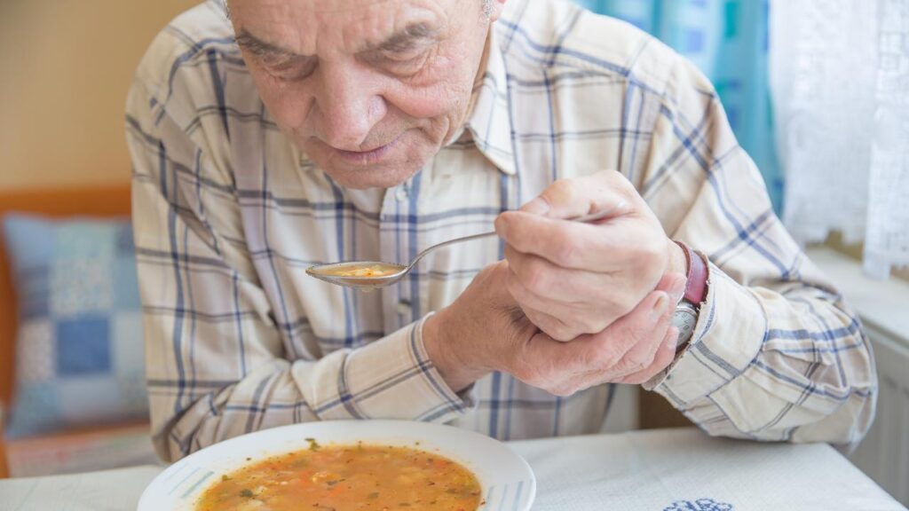 Uomo anziano con la malattia di Parkinson tiene il cucchiaio in entrambe le mani.